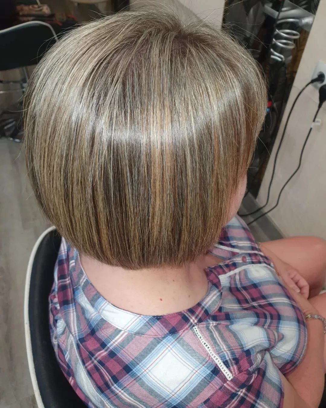 Mujer con un corte de cabello bob corto, liso y rubio con reflejos. Está sentada de espaldas, usando una camisa de cuadros.